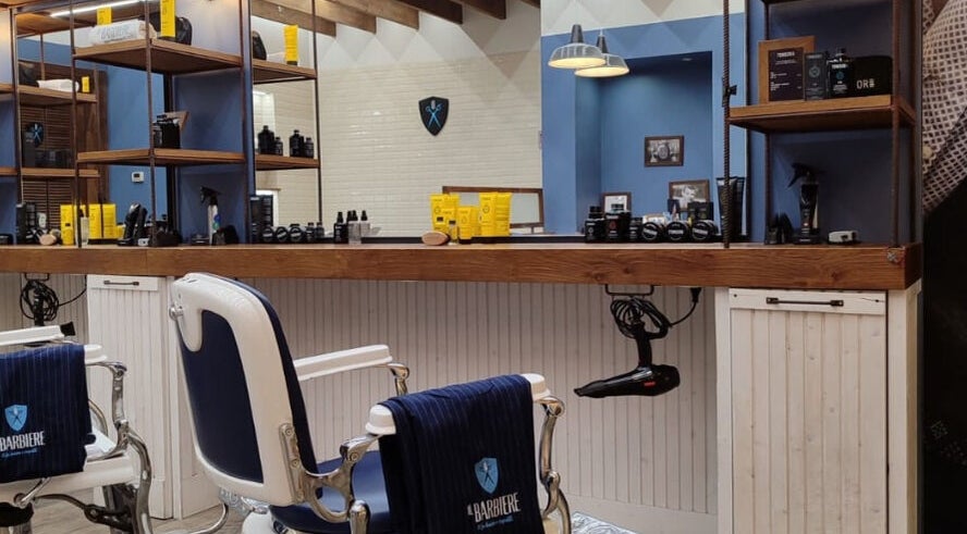 Interno moderno di Il Barbiere Cremona, situato a Cremona, Lombardia, IT con poltrone stilistiche e prodotti di bellezza.