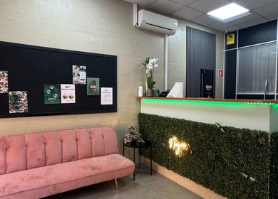 Recepción moderna en Nayco centro estético, Palma, Illes Balears, ES, con sofá rosa y decoración verde.