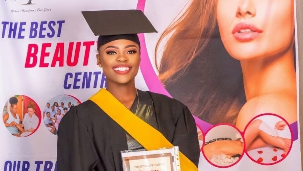 A happy graduate holds a certificate in front of a beauty center banner at Bots Massage Mobile, Cape Town, Western Cape, ZA.