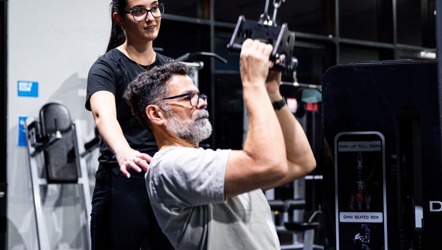 Instructor at LeanFit Performance, Birtinya guides a man using gym equipment.