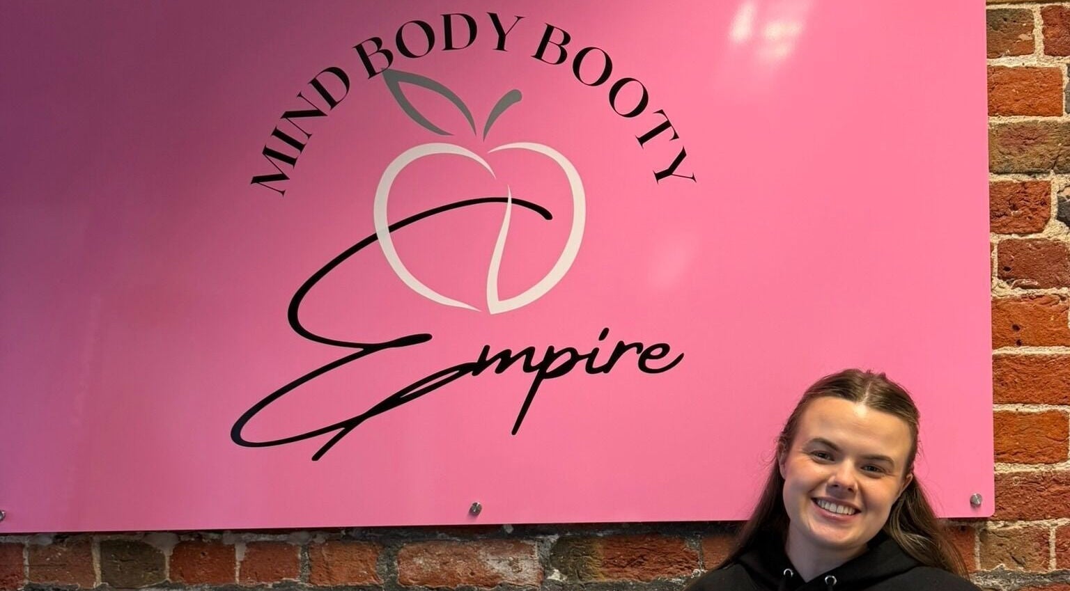Welcoming pink sign at Hayley's Health Hub in Knowsley, England, GB with smiling woman.
