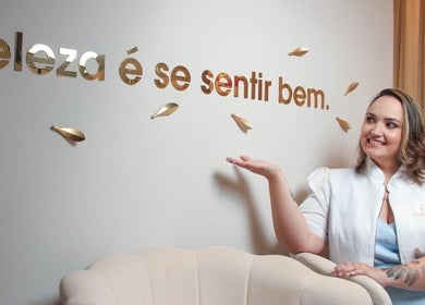 Profissional sorrindo no Guta Maciel, Minas Gerais, BR, com slogan 'Beleza é se sentir bem' na parede.