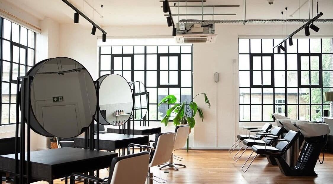 Modern salon interior at Hair By Ashley Rose, London, England, GB featuring sleek styling stations and bright windows.