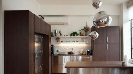 Modern kitchen area at Hair By Ashley Rose, London, England, GB featuring wooden cabinets and sleek countertops.