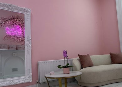 Elegant lounge area at Glow Up Beauty Studio, Dublin, County Dublin, IE, featuring a pink wall and plush sofa.