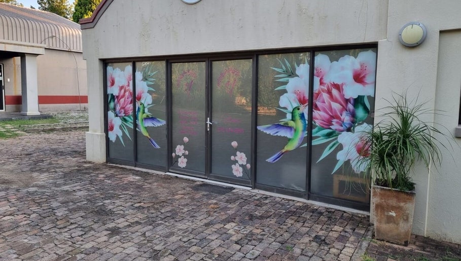 Colorful window art at The Look Hair Gallery, Potchefstroom, North West, ZA, showcasing hummingbird and flowers.