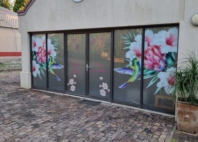 Colorful window art at The Look Hair Gallery, Potchefstroom, North West, ZA, showcasing hummingbird and flowers.