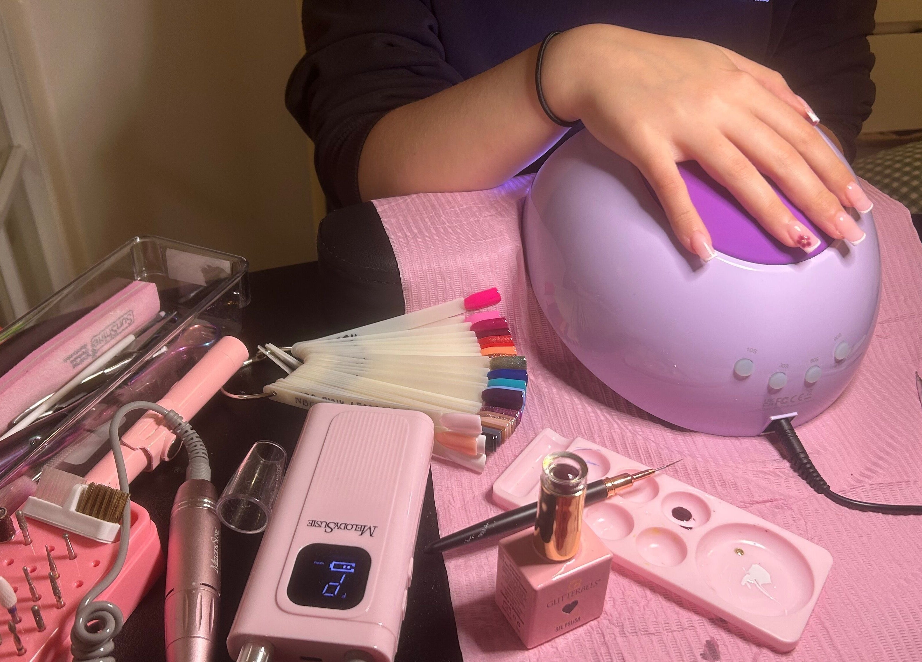 Hand receiving a manicure under a UV lamp at Popsiesmanis, Southampton, England, GB featuring tools and polish.