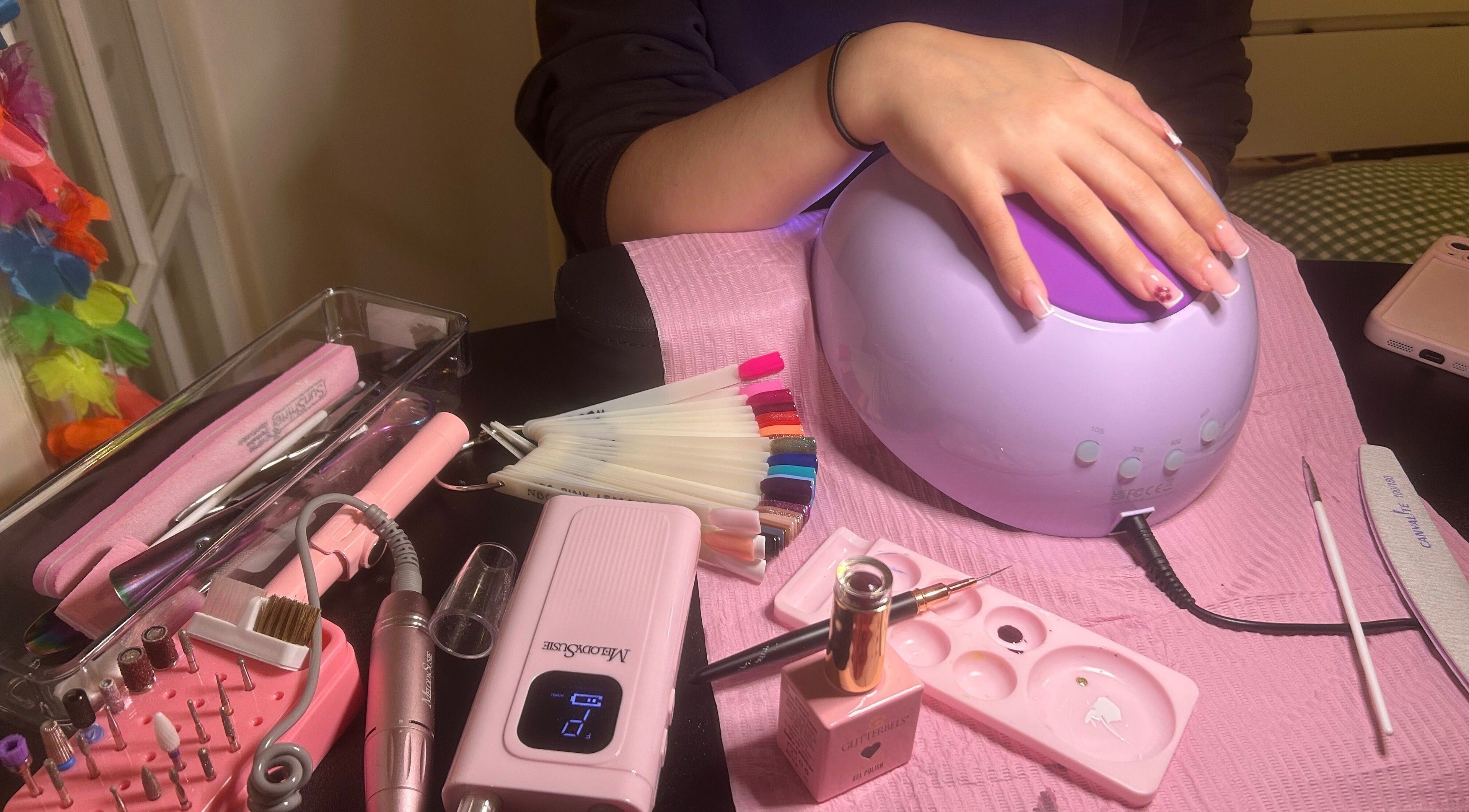 Hand receiving a manicure under a UV lamp at Popsiesmanis, Southampton, England, GB featuring tools and polish.