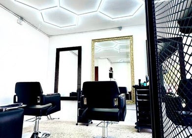 Interior moderno de O Cabelo, peluquería en Ciudad De México, MX, con sillas negras y espejos grandes.