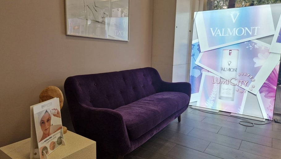 Sala de espera elegante en Cinc Estètica, Barcelona, Catalunya, ES con sofá púrpura y cartel de Valmont.