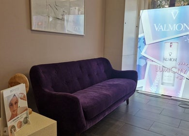 Sala de espera elegante en Cinc Estètica, Barcelona, Catalunya, ES con sofá púrpura y cartel de Valmont.