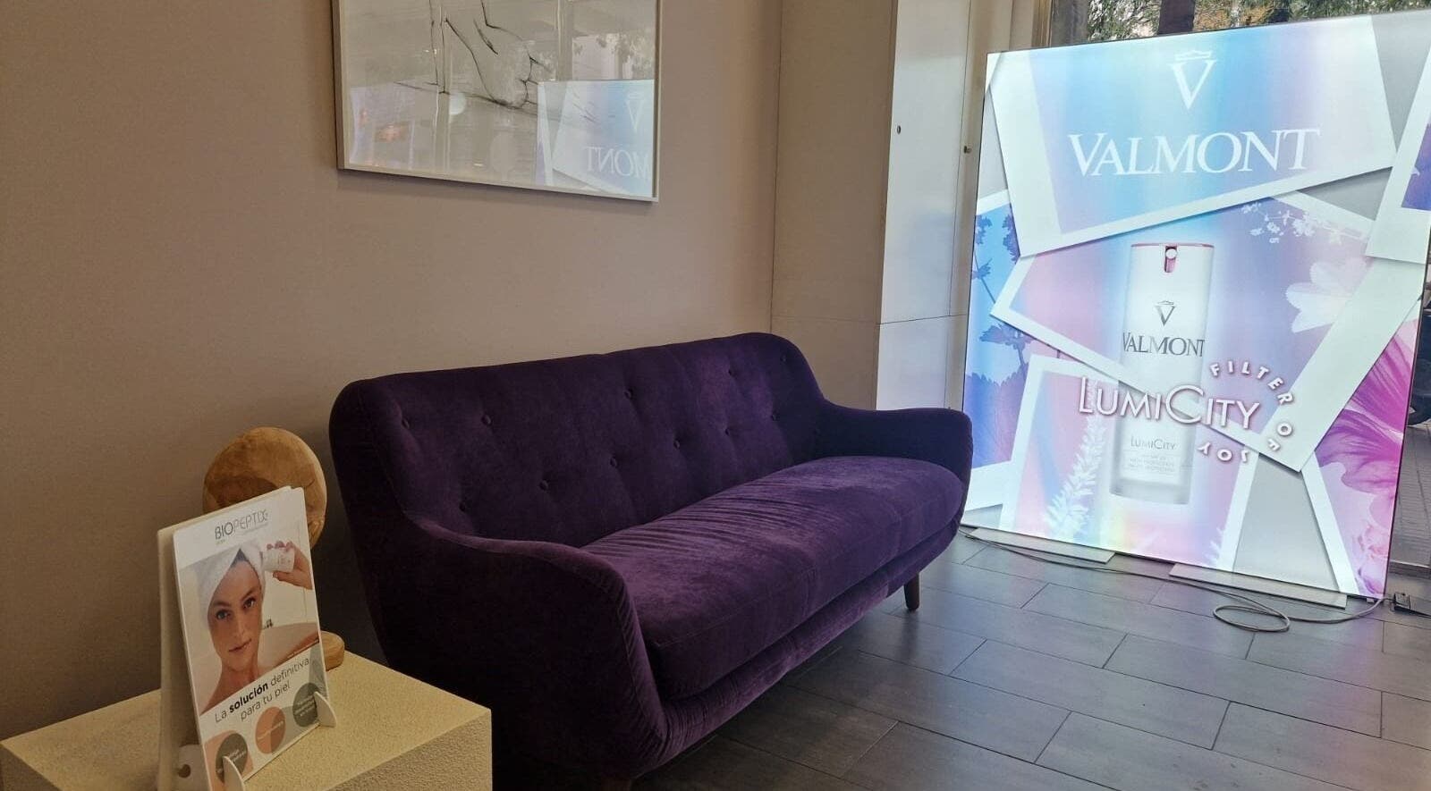 Elegante sofá violeta en Cinc Estètica, Barcelona, Catalunya, ES, con cartel publicitario de Valmont.