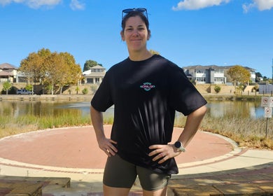 Smiling person in Cruz S&C shirt, Yangebup, Western Australia, AU, with serene lake backdrop.