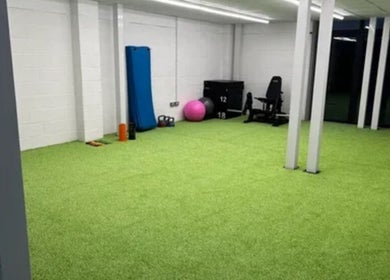 Spacious fitness room at True Form Therapy Ltd in Three Legged Cross, England, GB, with gym equipment and bright green floor.