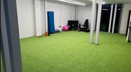 Spacious fitness room at True Form Therapy Ltd in Three Legged Cross, England, GB, with gym equipment and bright green floor.