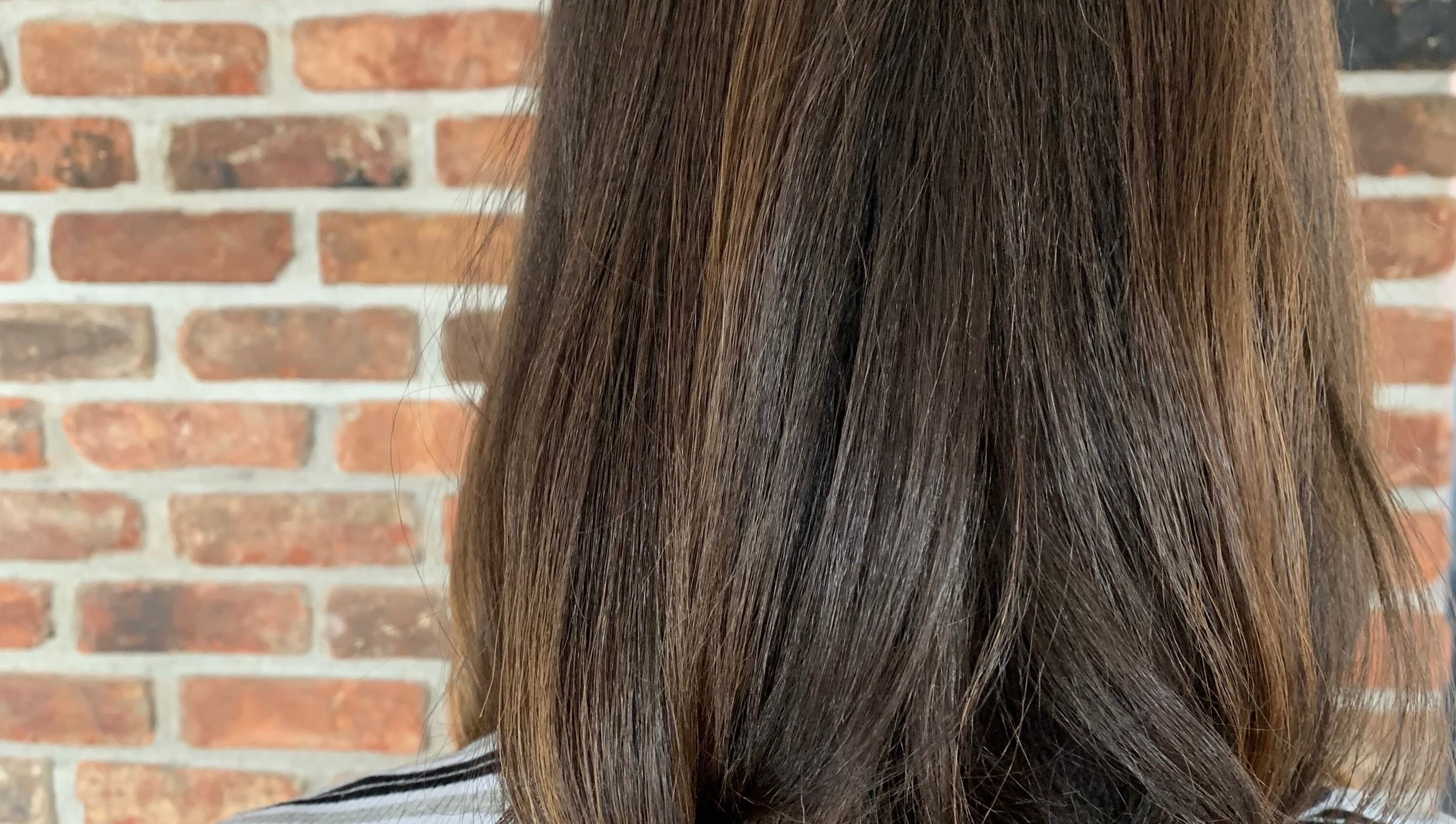 Sleek brunette hairstyle at You.360bda, City Of Hamilton, Pembroke Parish, BM with a brick wall backdrop.