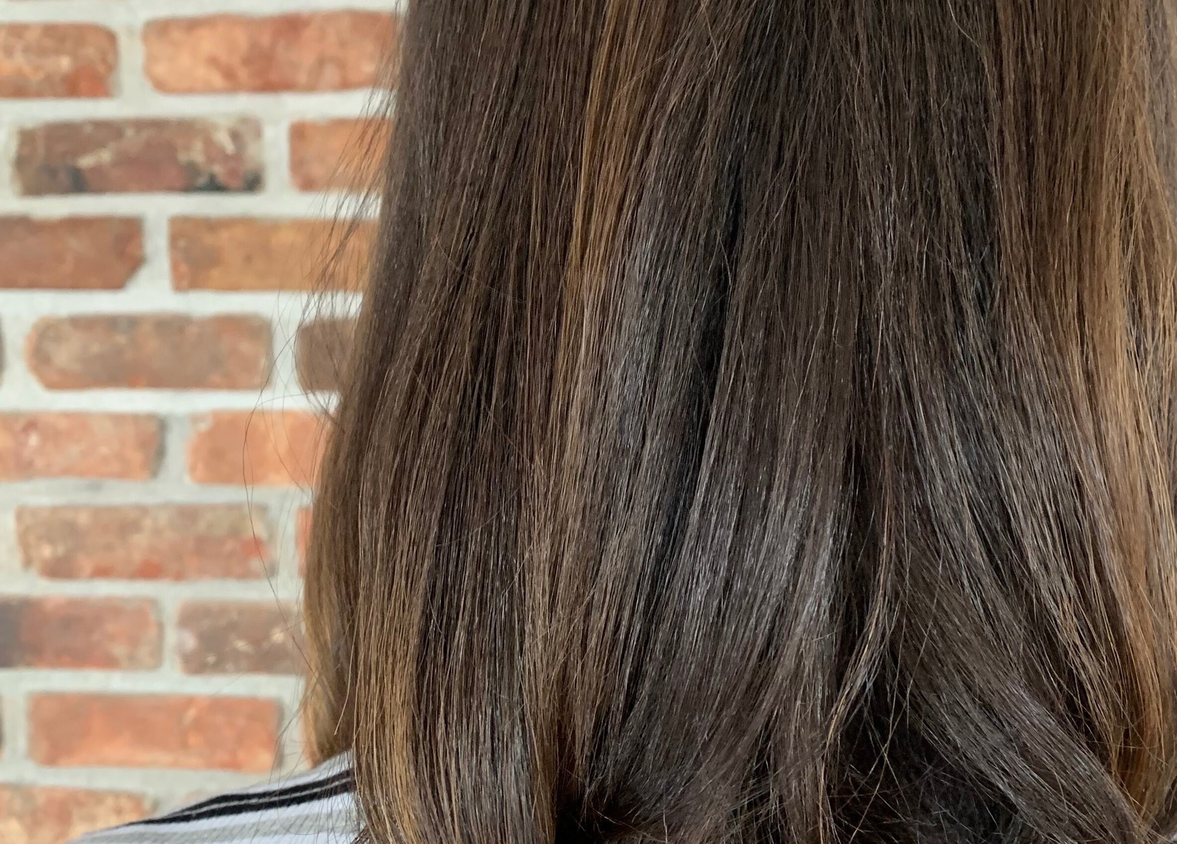 Sleek brunette hairstyle at You.360bda, City Of Hamilton, Pembroke Parish, BM with a brick wall backdrop.