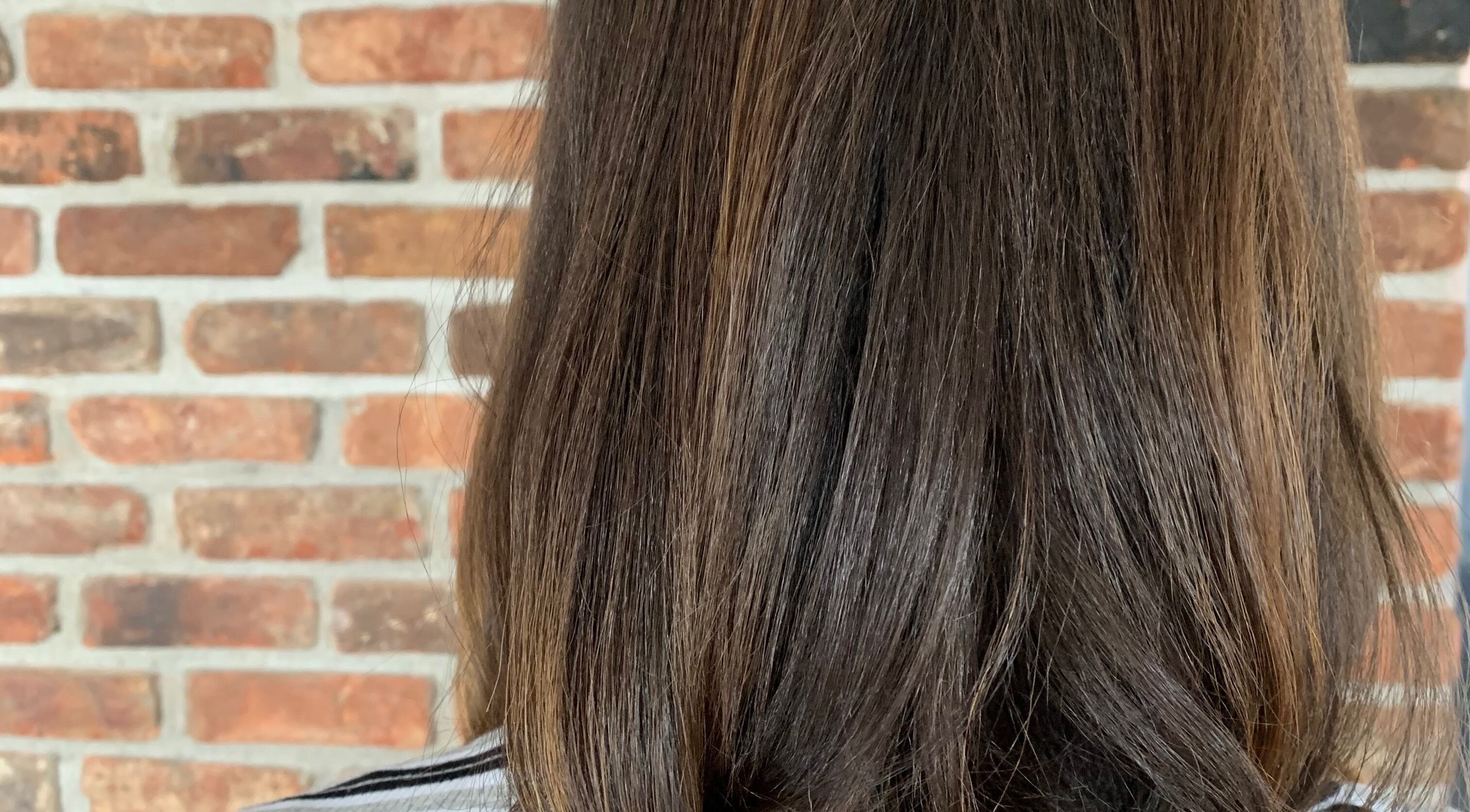 Sleek brunette hairstyle at You.360bda, City Of Hamilton, Pembroke Parish, BM with a brick wall backdrop.