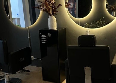 Interior de D`LART SALON en Medellín, Antioquia, CO con espejos circulares iluminados y sillas estilizadas.