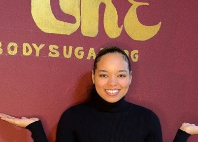 Smiling individual at Pure Body Sugaring holding out hands in Willemstad, Curaçao, CW with logo in background.