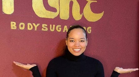 Smiling individual at Pure Body Sugaring holding out hands in Willemstad, Curaçao, CW with logo in background.