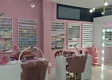 Elegante salón de uñas en The Nails Room, Ciudad Sahagun, MX, con estantes de esmaltes coloridos y espejos iluminados.