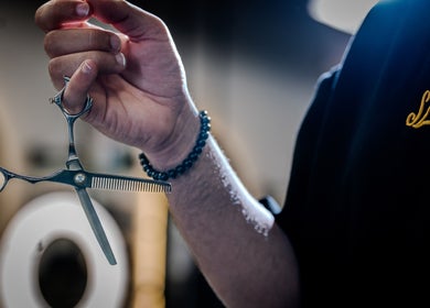 Barber holding scissors at Sleek Care, Riyadh, Riyadh Province, SA, highlighting professional grooming services.