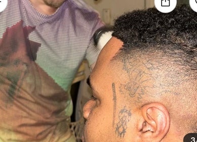 Barber at Payso Cuts in New York, New York, US giving a precise haircut to a client with intricate tattoos.