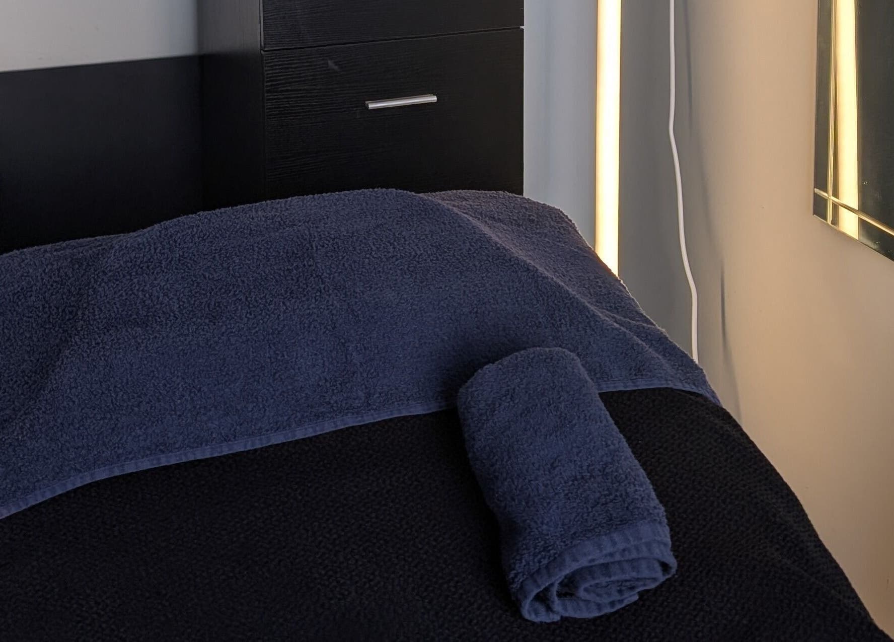 Cozy massage room setup at Massage by Sam, Stourbridge, England, GB, with dark towels and ambient lighting.