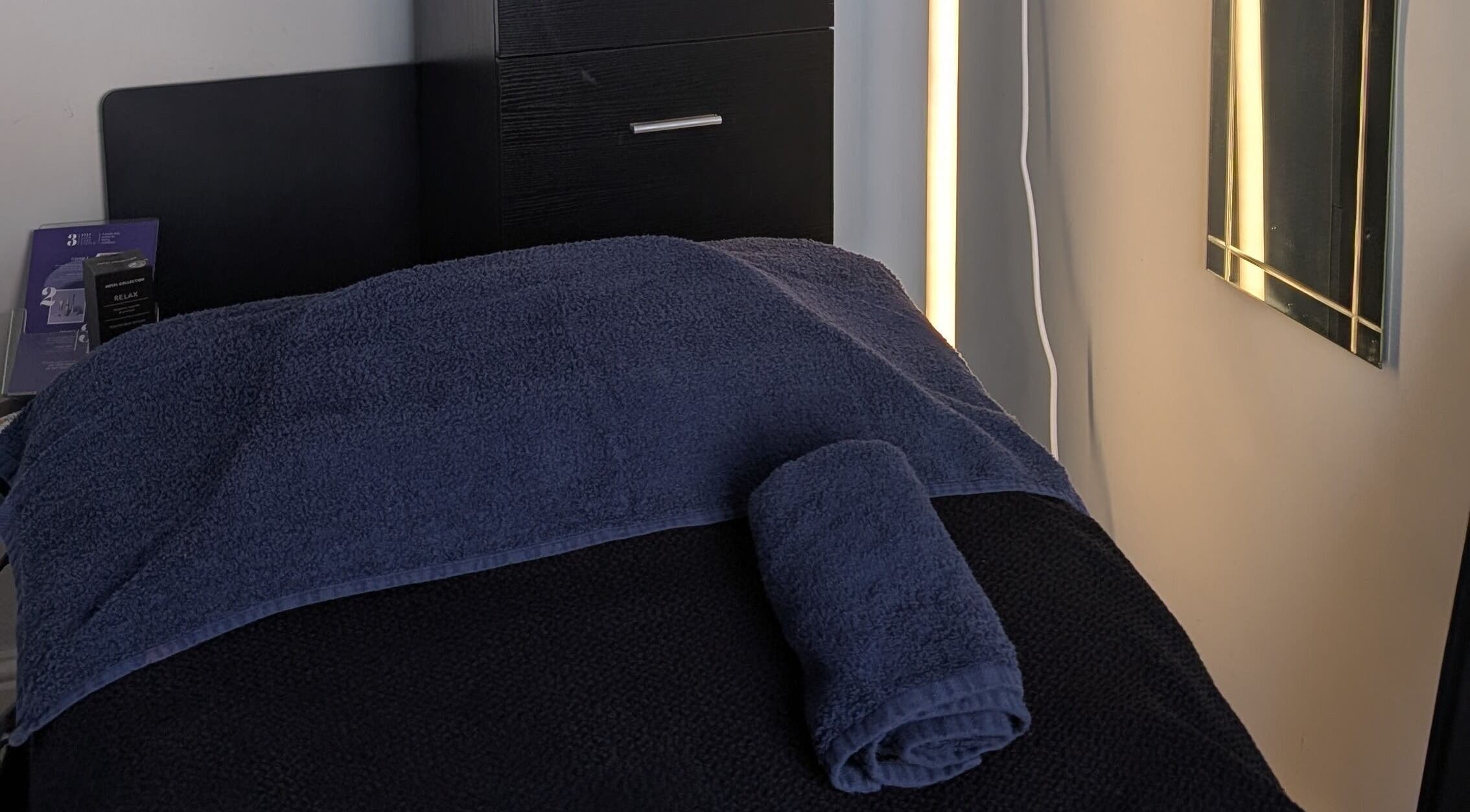Cozy massage room setup at Massage by Sam, Stourbridge, England, GB, with dark towels and ambient lighting.