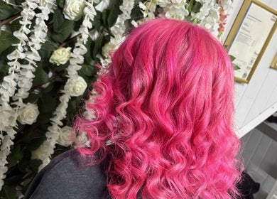 Vibrant pink wavy hair styled at Roots & Rebel, Ellesmere Port, England, GB, with floral background.