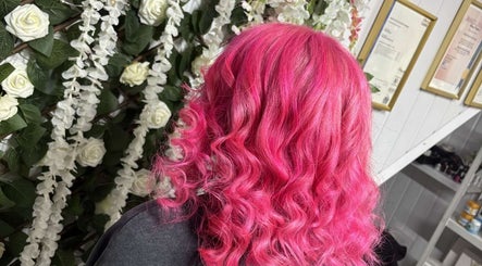 Vibrant pink wavy hair styled at Roots & Rebel, Ellesmere Port, England, GB, with floral background.