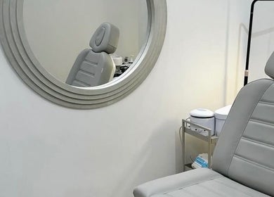 Modern treatment room with gray chair and round mirror at Reset Beauty, London, England, GB.