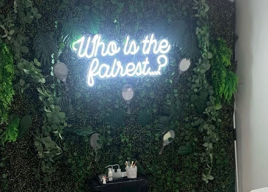 Lush greenery wall with neon 'Who is the fairest?' at Ash Fern Tattoo, Romford, England, GB.