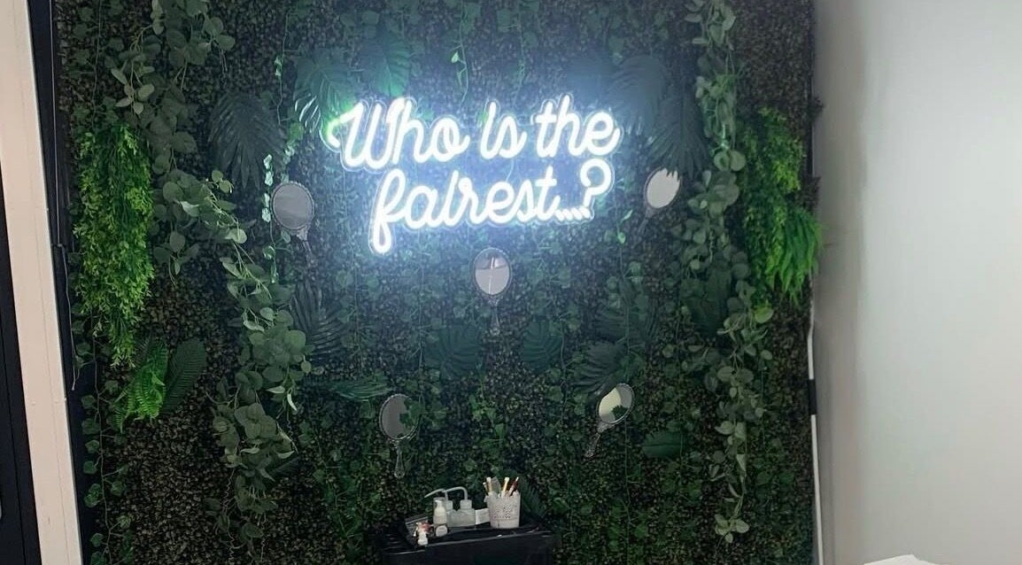 Lush greenery wall with neon 'Who is the fairest?' at Ash Fern Tattoo, Romford, England, GB.