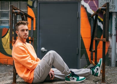 Person in orange sweater sits against vibrant mural near Nails By Adela in Eugene, Oregon, US.