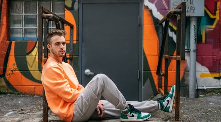 Person in orange sweater sits against vibrant mural near Nails By Adela in Eugene, Oregon, US.