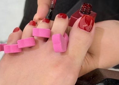 Red toenails being painted at Bella Naillash, Manchester, England, GB. Relaxing pedicure service.