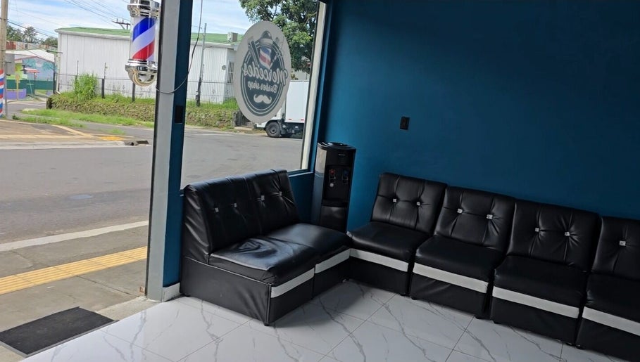 Comfortable seating at Mercedes Barber Shop, Barva, Heredia, CR, featuring stylish black sofas.
