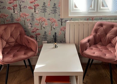 Inviting blush seating area at GLAMMY, London, England, GB with chic wallpaper and cozy chairs.