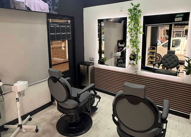 Interior moderno de EME BARBER STUDIO en Zaragoza, Aragón, ES, con sillones de barbero y plantas decorativas.