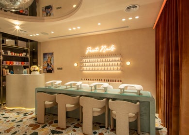 Elegant nail lounge at Beauty Club London, Dubai. Modern decor with beige chairs and neon sign.