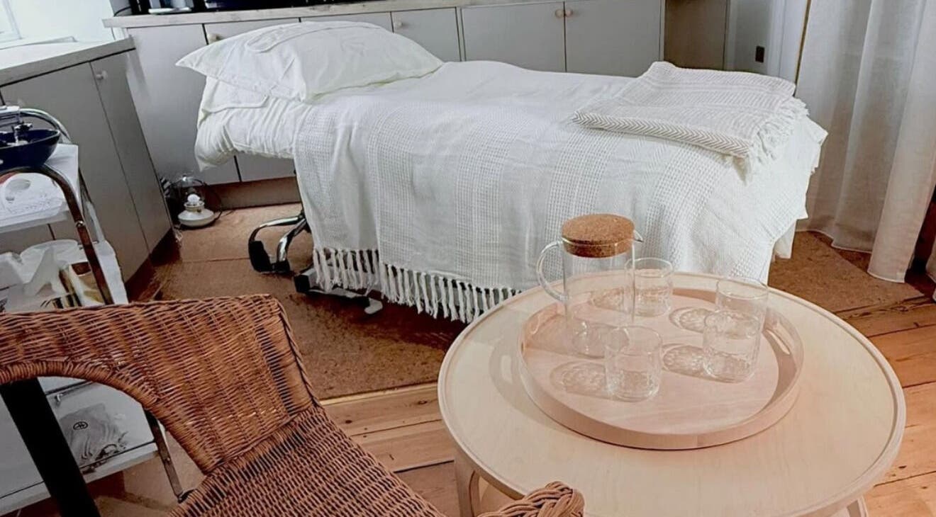 Welcoming massage room at Qui Yoga & Ayurveda in Topsham, England, GB with a cozy bed and wicker chair.