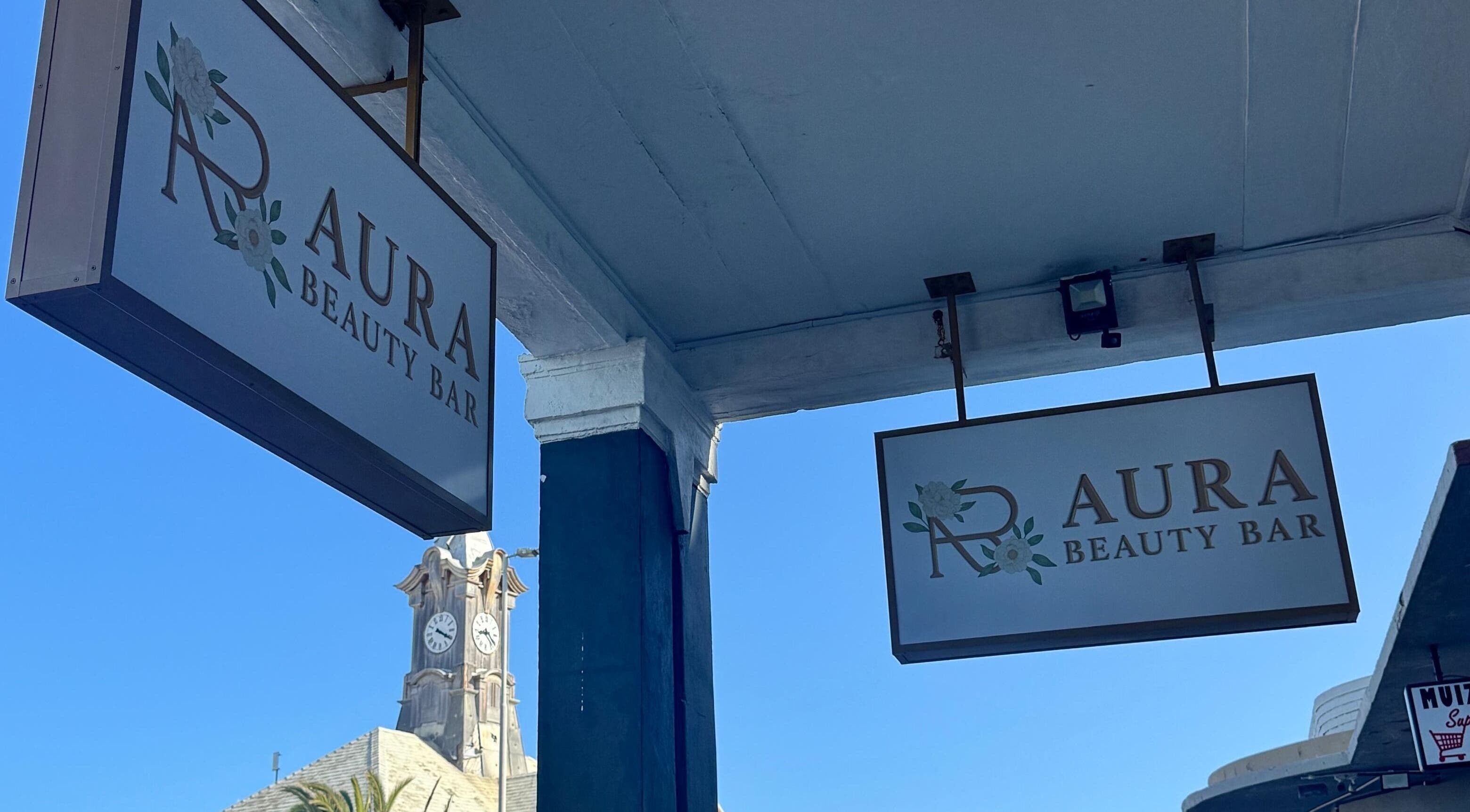 Entrance signs of AURA BEAUTY BAR in Cape Town, Western Cape, ZA under a clear sky.