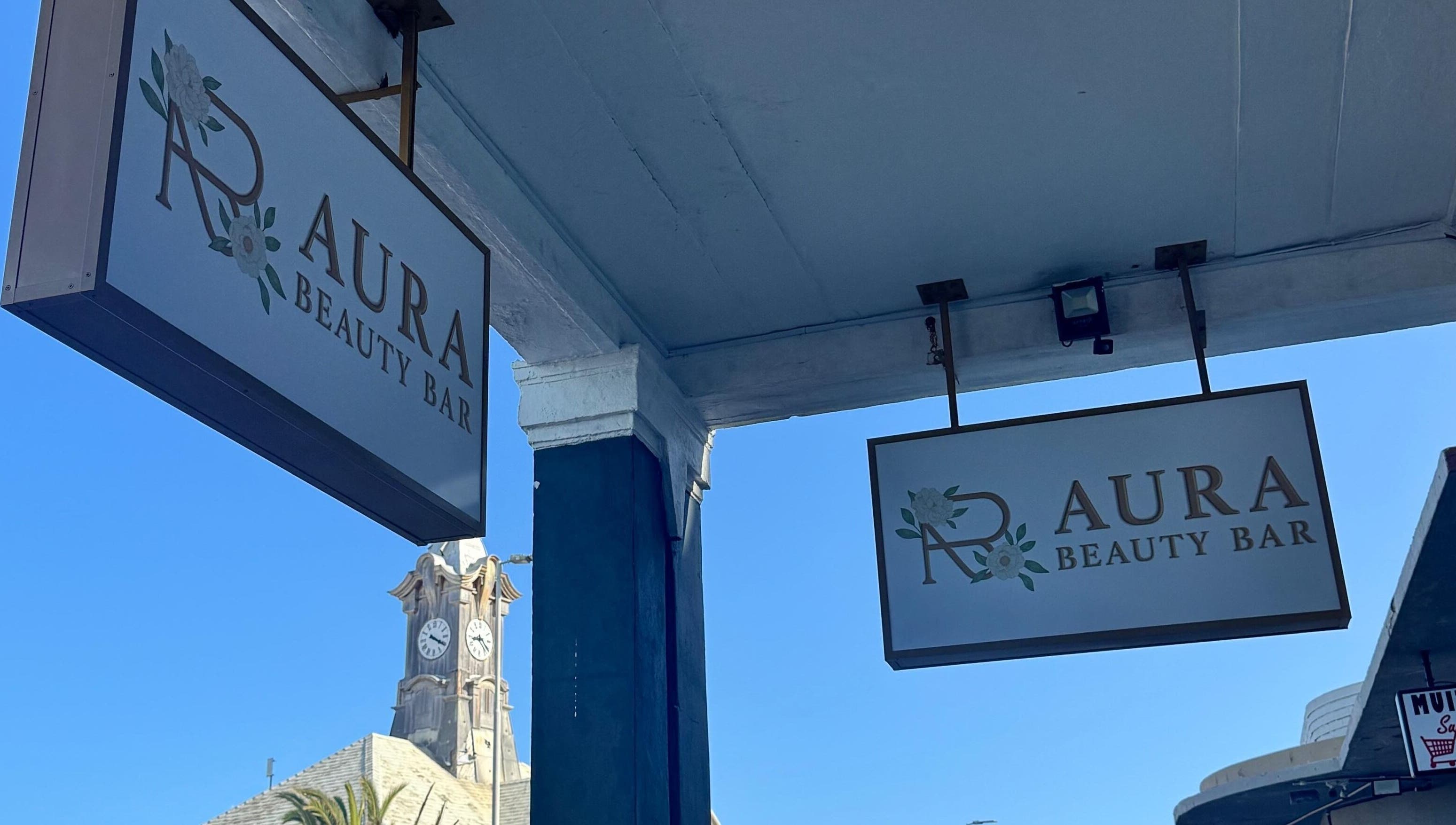 Signs outside AURA BEAUTY BAR, Cape Town, Western Cape, ZA under clear blue sky.