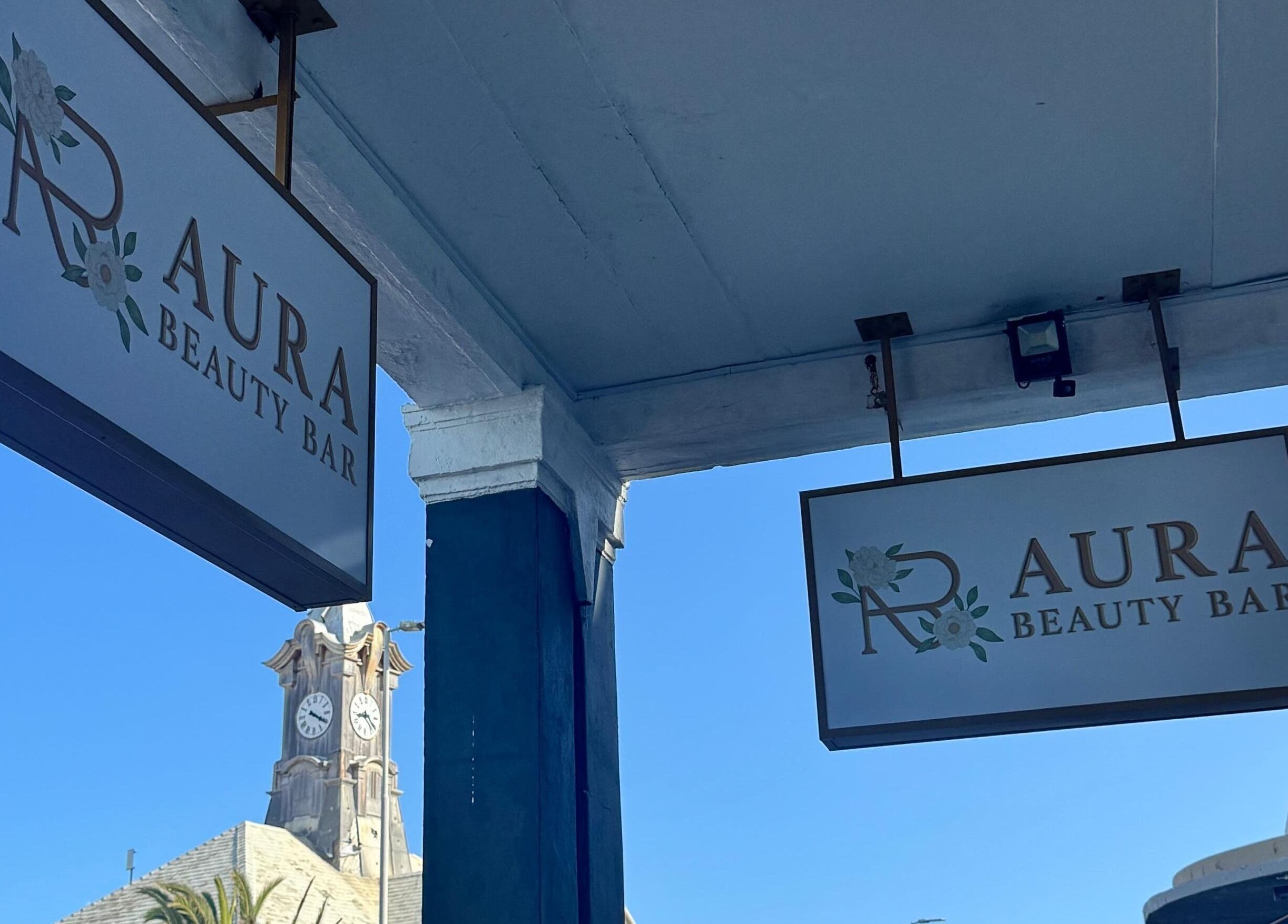 Signs outside AURA BEAUTY BAR, Cape Town, Western Cape, ZA under clear blue sky.