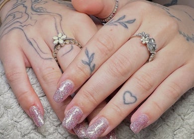 Sparkling glitter nails at Lluxury Nails, Weston-super-Mare, England, GB with delicate tattoo art and rings.