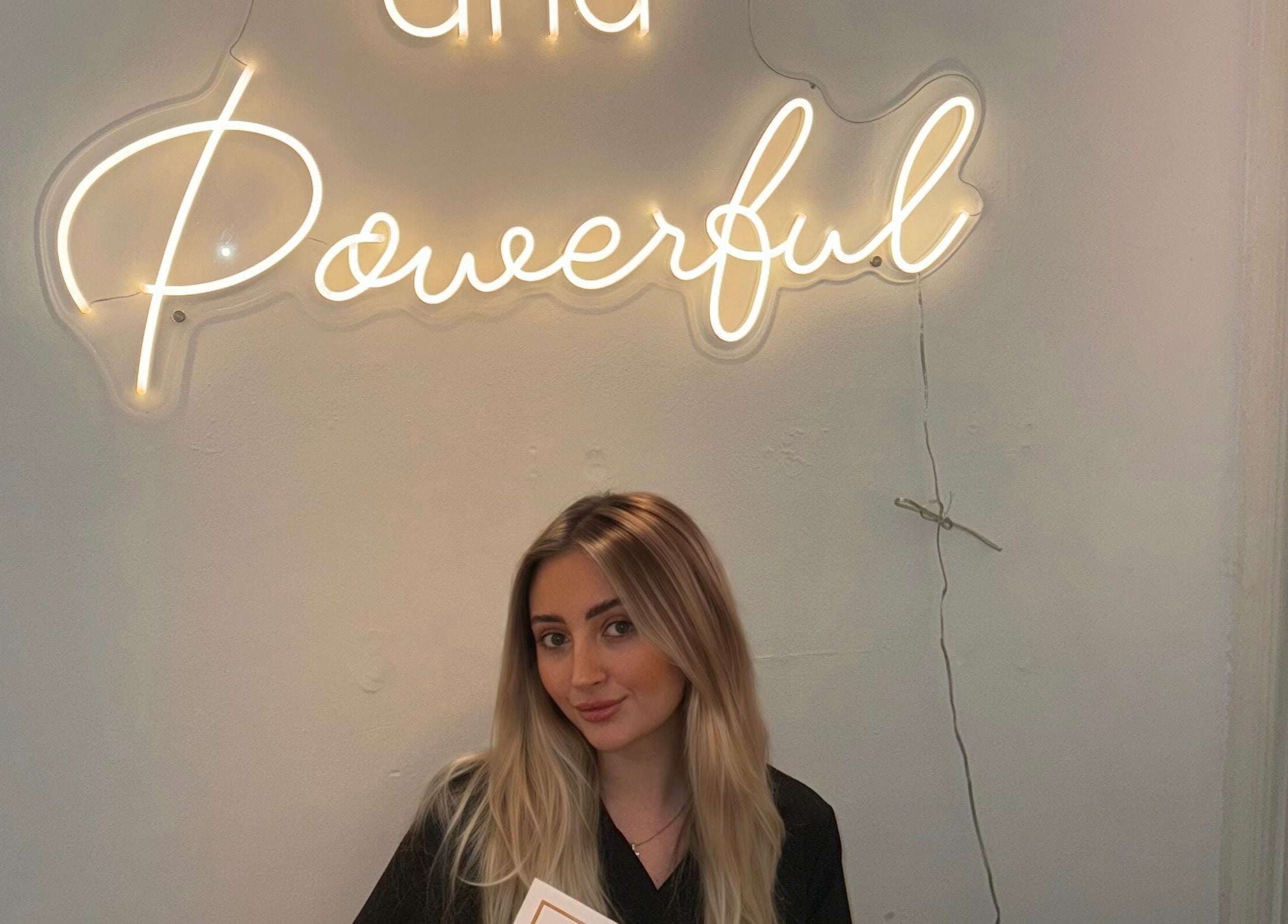 Smiling woman at Daly Aesthetics under neon sign, Little Hulton, England, GB.