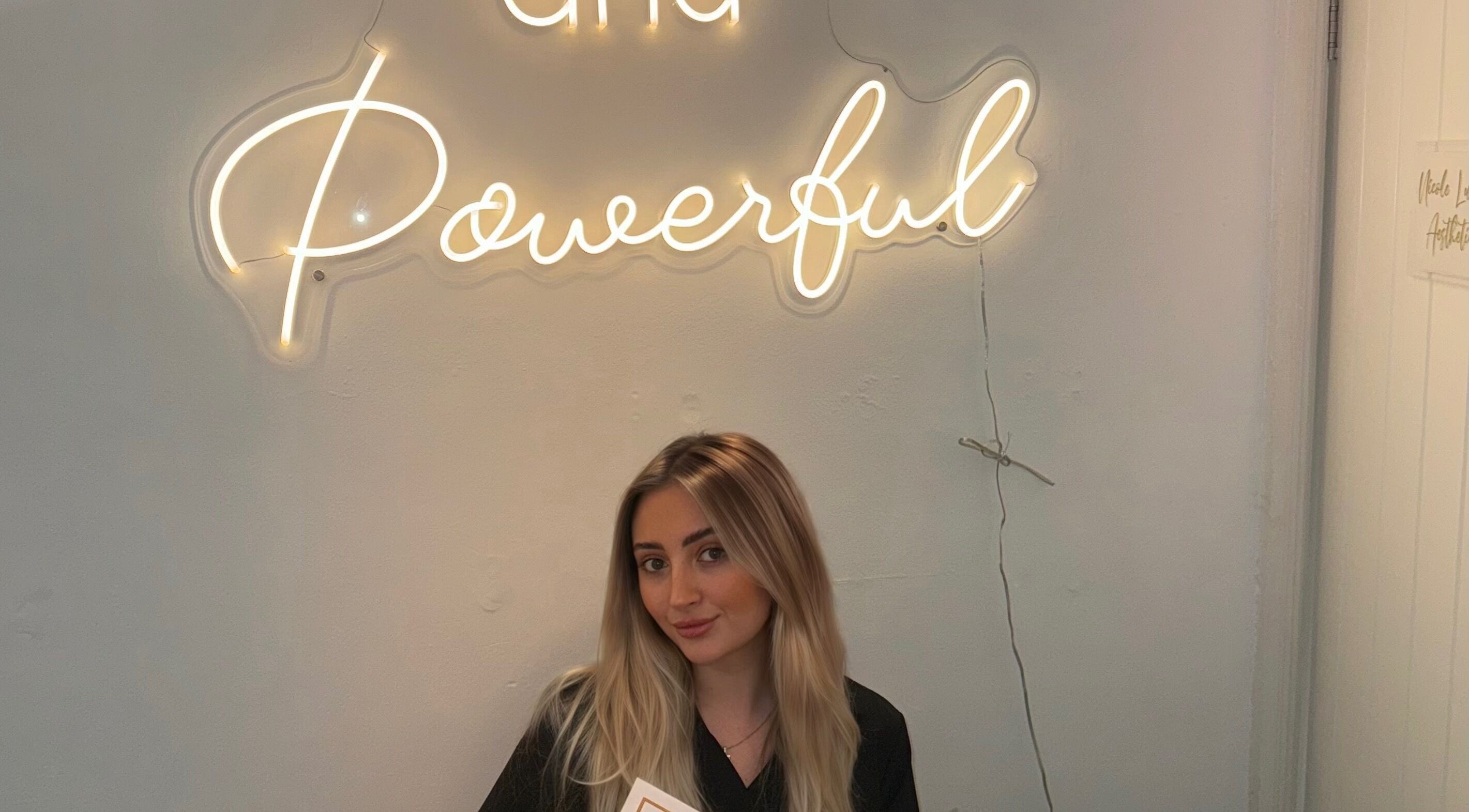 Smiling woman at Daly Aesthetics under neon sign, Little Hulton, England, GB.